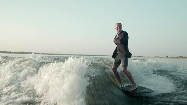 A surfer jumping on a wakeboard in a suit. An experienced wakeboarder sprays water drops into the camera.