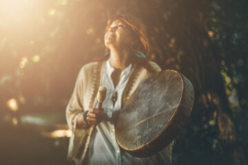 shamanic woman playing on shaman frame drum in the nature.