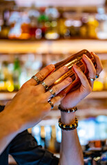 man at bar holds steel shaker in her hands, shakes it to make cocktail.