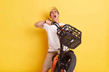 Indoor shot of man wearing cap and t shirt riding on electric e scooter, collision accident, funny man with scared facial expressing, full of fear, screaming while falling down from electric bike.