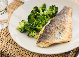 fried fillet of sea bass with garnish of broccoli on black warm stone plate