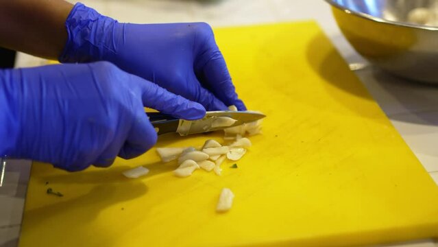 gloved hands cut garlic into small pieces. preparation of spicy food.