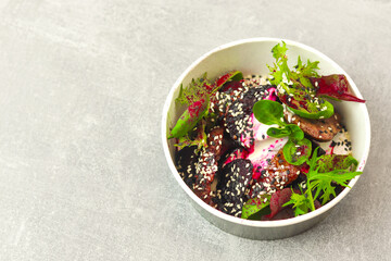 Salad of lettuce, beet and chicken liver with fresh radicchio and sesame seeds in a takeaway round container topped with yoghurt sauce on gray background. Healthy food delivery concept.