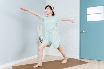 家でヨガ・ピラティス・ストレッチをするおしゃれな日本人女性（英雄のポーズ）
