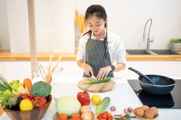 Attractive asian woman cutting cucumber at kitchen