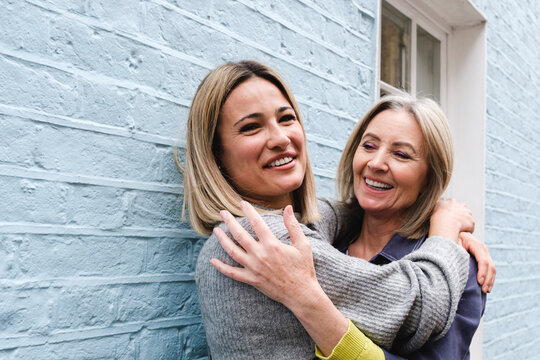 Happy young woman embracing mother in front of blue wall