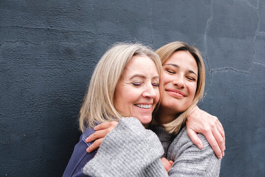 Smiling mother and daughter with eyes closed embracing each other