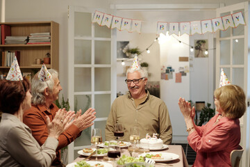 Happy senior man looking at his friends clapping hands by dinner table served with homemade food...