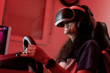 Man wearing VR glasses playing video games with steering wheel at home