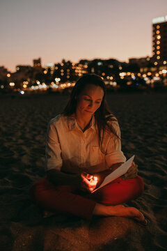 Woman burning paper with cigarette lighter sitting on beach at night