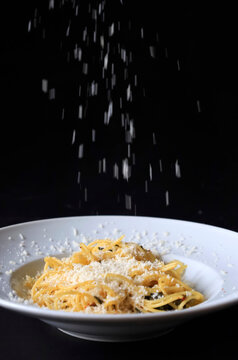 Studio shot of grated Parmesan pouring on plate of pasta