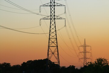 Silueta de torres de alta tensión para la conducción de electricidad. Imagen tomada al atardecer con los últimos rayos del sol mientras se pone en el horizonte. Madrid, España.