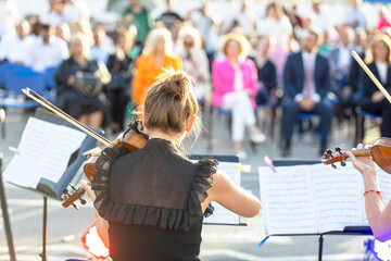 Musician playing violin at classical music concert or outdoors event in front of blurred audience