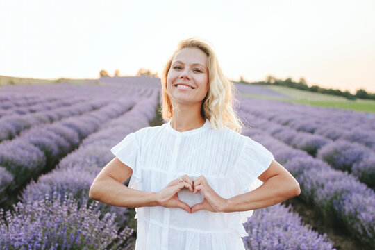 Happy woman gesturing heart shape standing in lavender field
