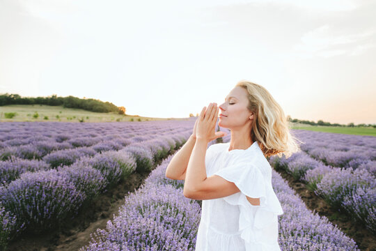 Smiling woman with hands clasped praying in lavender field