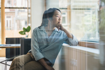 Businesswoman with hand on chin seen through glass of office