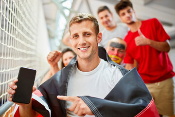 Smiling man with German Flag pointing at smart phone screen at sports event in stadium