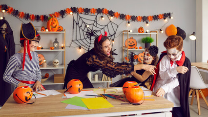Overjoyed young teacher and kids dressed in costumes engaged in learning activity on Halloween eve. Happy nanny have fun play with kids celebrate scary all saint eve in school or kindergarten.