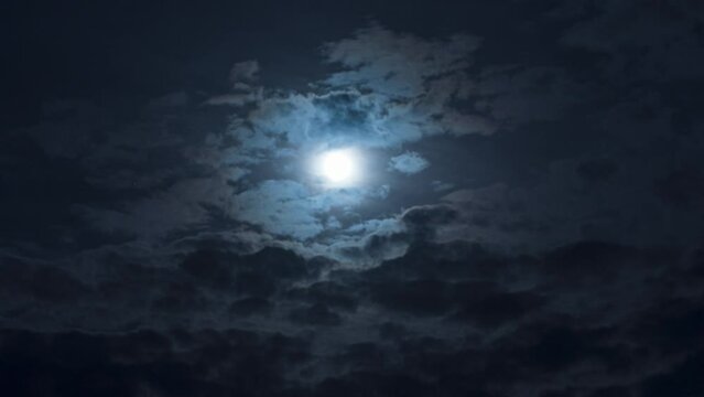 A mysterious night sky with clouds and a full moon. Nighttime timelapse. Clouds cover and reveal the moon
