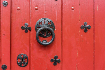 Porte en bois peinte en rouge ancienne avec un heurtoir rond