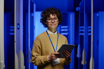 Portrait of female engineer in eyeglasses looking at camera while working on digital tablet in server room - Powered by Adobe