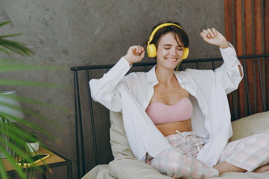 Young woman wear white shirt pajama headphones she lying in bed listen to music dancing rest relax spend time in bedroom lounge home in own room hotel wake up dream be lost in reverie good mood day