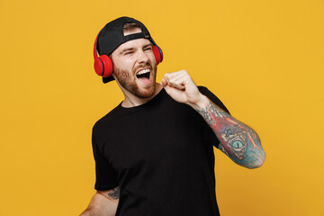 Young happy bearded tattooed man 20s he wear casual black t-shirt cap headphones listen to music...