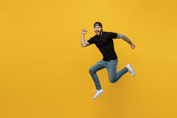 Fototapeta na wymiar Full body side view sporty strong young bearded tattooed man 20s he wears casual black t-shirt cap jump high run fast isolated on plain yellow wall background studio portrait People lifestyle concept