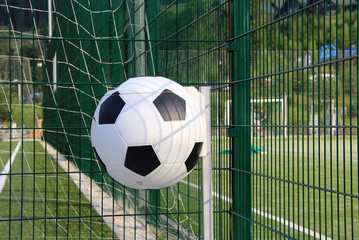 Round trash can in the shape of a football ball near fence of a soccer field
