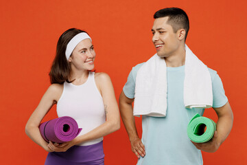 Young happy fitness trainer instructor sporty two man woman in headband t-shirt hold yoga mat look to each other spend weekend in home gym isolated on plain orange background. Workout sport concept. - obrazy, fototapety, plakaty