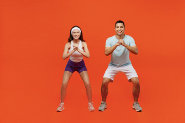 Full body smiling fun young fitness trainer instructor sporty two man woman in headband t-shirt do squat spend weekend in home gym isolated on plain orange background. Workout sport lifestyle concept.