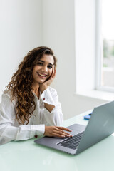Young beautiful joyful woman smiling while working with laptop in office