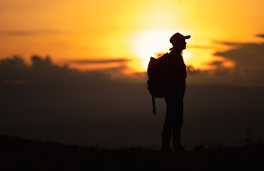 Young woman with backpack hikes in the mountain with a beautiful view through the sunset and warm red light. Blurred silhouette background.