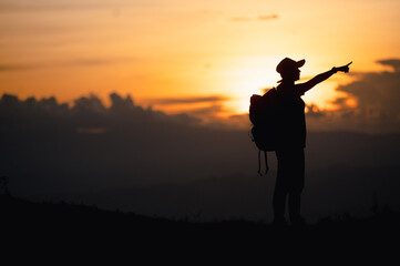 Young woman with backpack hikes in the mountain with a beautiful view through the sunset and warm red light. Blurred silhouette background.
