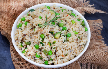 Wild and brown rice pilaf with green peas, onion and baby marrow on black slate with burlap 