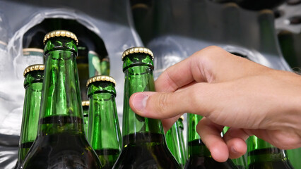 Close-up of many green glass bottles of beer on a store shelf and a male hand takes one