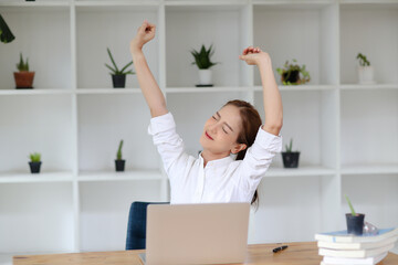 young Asian women feel tired from hard work, thus doing arm stretching posture to relax body. Tired Asia woman stretching her hands while working in office.