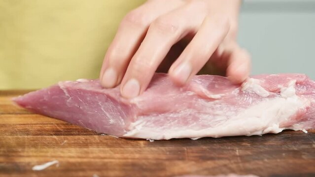 The chef cuts raw pork tenderloin with the knife.
