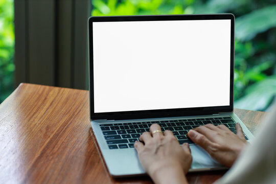 woman using and typing on laptop computer with blank white desktop screen on wooden table