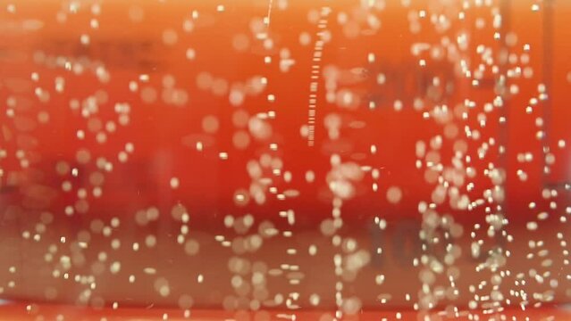 Macro shot of air bubbles in prosecco rising up on the red background.
