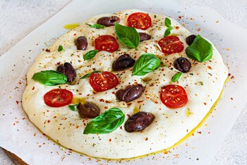Fresh Italian flat bread (raw) Focaccia with tomatoes, olives, garlic and herbs on a wooden background.