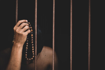 male inmate in prison with bead in hand raises his hand to make a wish and pray on black background.concept for prisoner,sadness,detain,erroneousness