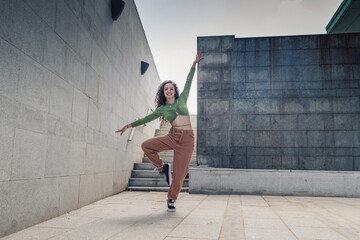 Young and attractive woman dancing freestyle dance in front of an urban and modern building stairs