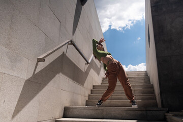 Young and attractive woman dancing freestyle dance in front of an urban and modern building stairs