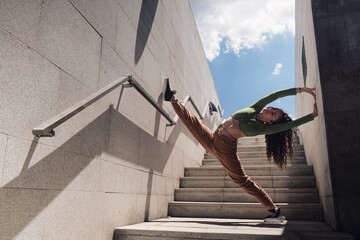 Young female gymnast doing splits on stairs of a modern building