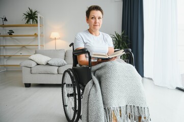 Shot of a senior woman sitting in a wheelchair and reading book at home