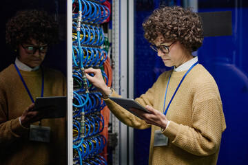 Serious IT engineer in eyeglasses looking at screen of digital tablet and checking the work of...