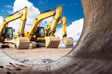 Powerful excavators at a construction site viewed from a large diameter pipe. earth moving construction equipment. Lots of excavators. Laying of underground communications.