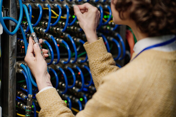 Close-up of young female engineer connecting wires in server cabinet while working with...