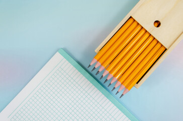 set of graphite pencils in an open wooden box and an empty blank on blue background. Pencils in pencil case and notebook sheet in cage. Banner, space for text. Back to School concept, top view - Powered by Adobe